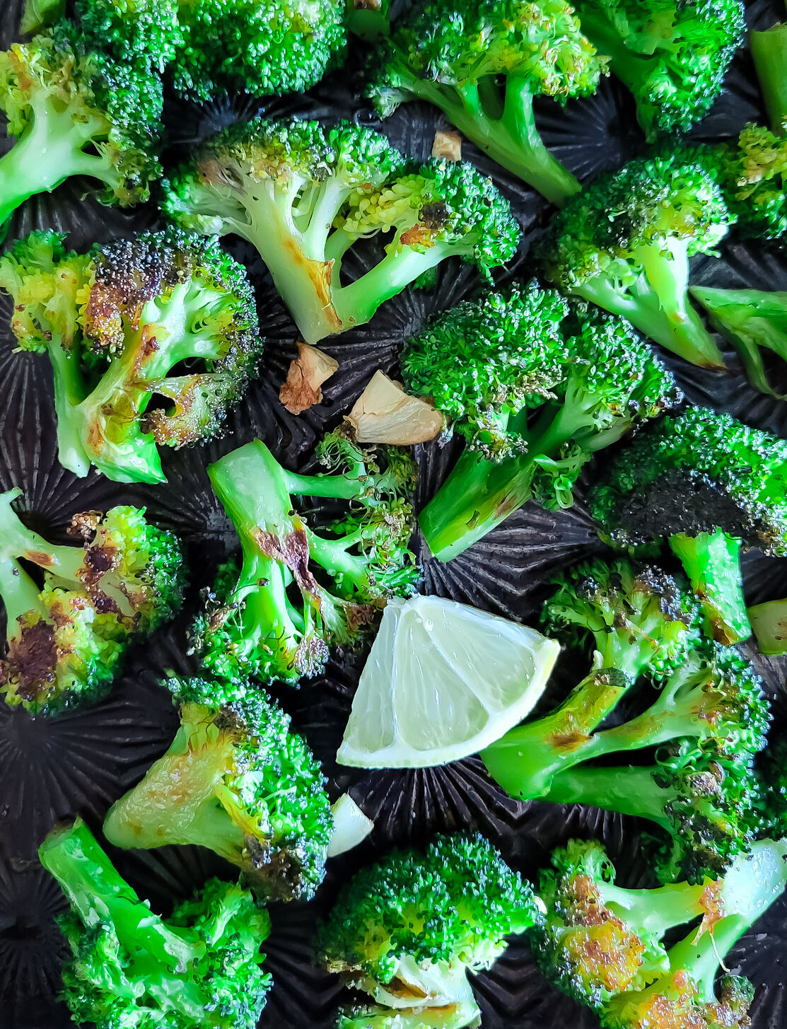 A sheet pan filled with roasted broccoli florets and a wedge of lemon.