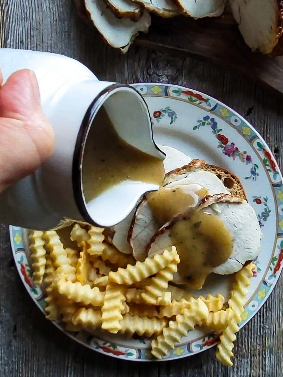 A plate with a hot turkey sandwich and crinkle fries is getting gravy poured over the sandwich and fries.