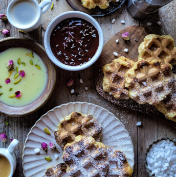 A tablescape of plates and cutting board loaded with Liege Mochi Waffles, white and dark chocolate dipping sauces, and espresso.