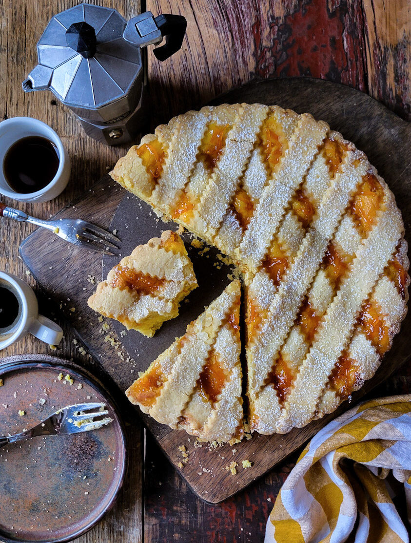 Sliced Marmalade Ricotta Crostata on a cutting board, with one slice half eaten, and espresso and plates to the side.