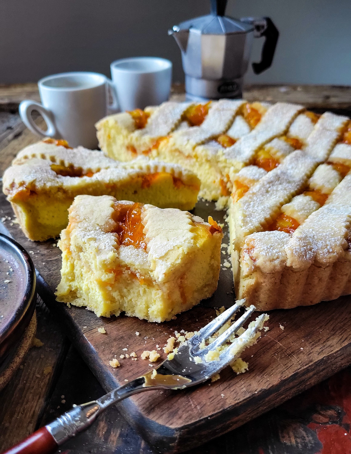 A Marmalade Ricotta Crostata sliced on a cutting board, ready to eat, with coffee in the background