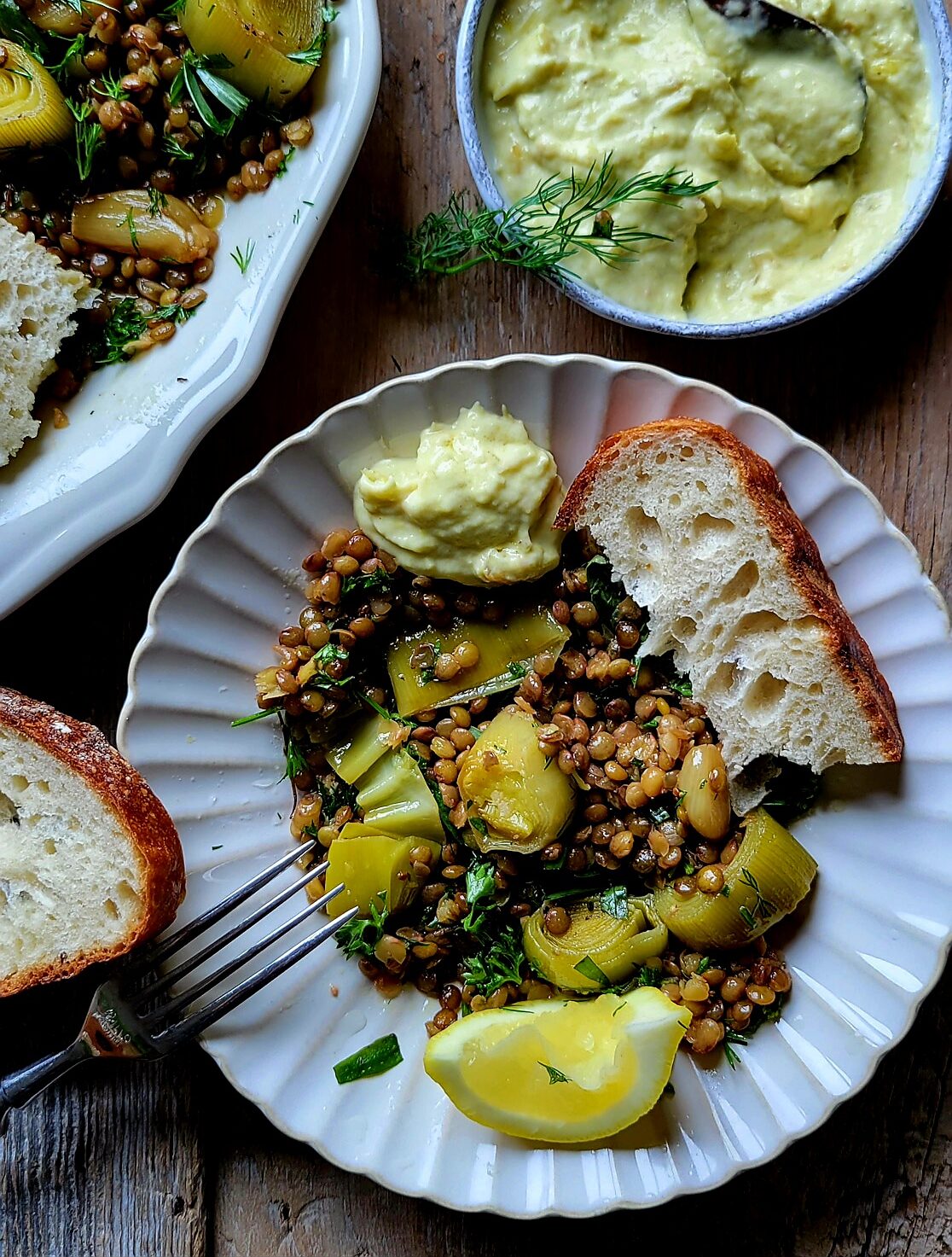 A plate filled with Leek Confit and Lentils with crusty bread and extra Leek cream to the side.