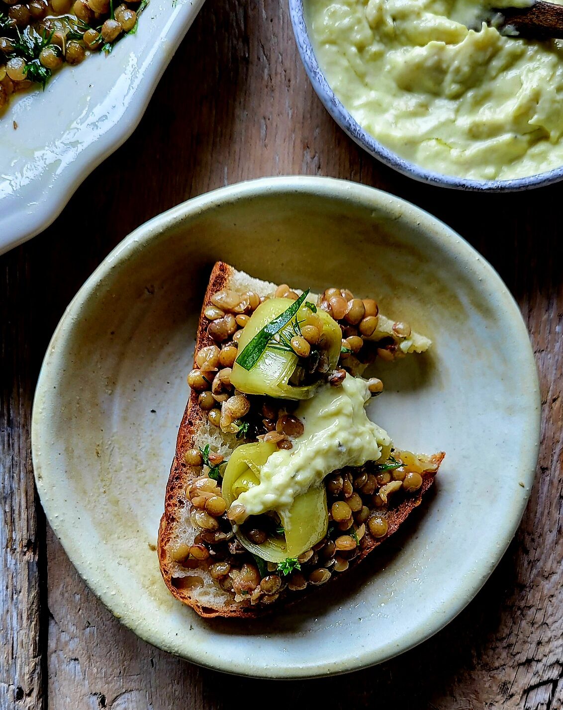 A plate with Leek Confit and lentils spread on crusty bread, topped with Leek Cream.