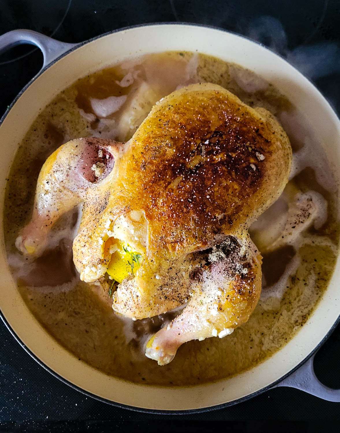 A pot filled with a seared chicken and broth about to go into the oven to braise.