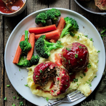 A plate filled with Brown Butter Mashed Potatoes, with two large glazed Turkey Meatloaf Balls on top, with steamed veggies to the side. A small bowl with extra glaze is to the side.