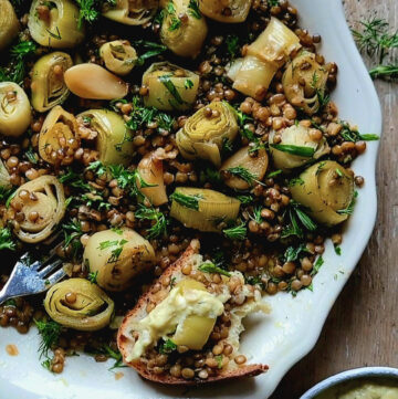 A platter filled with Leek Confit with Lentils. A piece of crusty bread topped with the leeks and lentils is to the side.