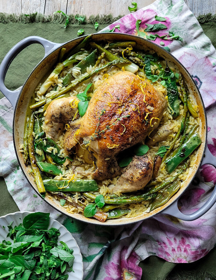 A pot filled with Spring Chicken and Orzo, and charred spring vegetables, with a plate of spring greens to the side.