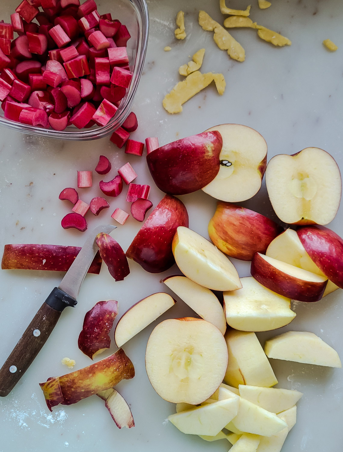 Sliced and peeled apples, and a bowl of cut up rhubarb for an Apple Rhubarb Pie