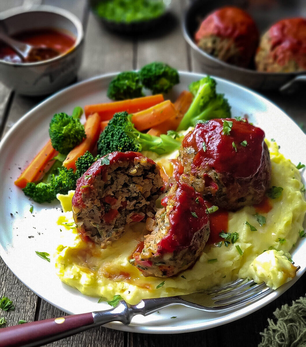 A plate filled with Brown Butter Mashed Potatoes, with two large glazed Turkey Meatloaf Balls on top, with steamed veggies to the side.