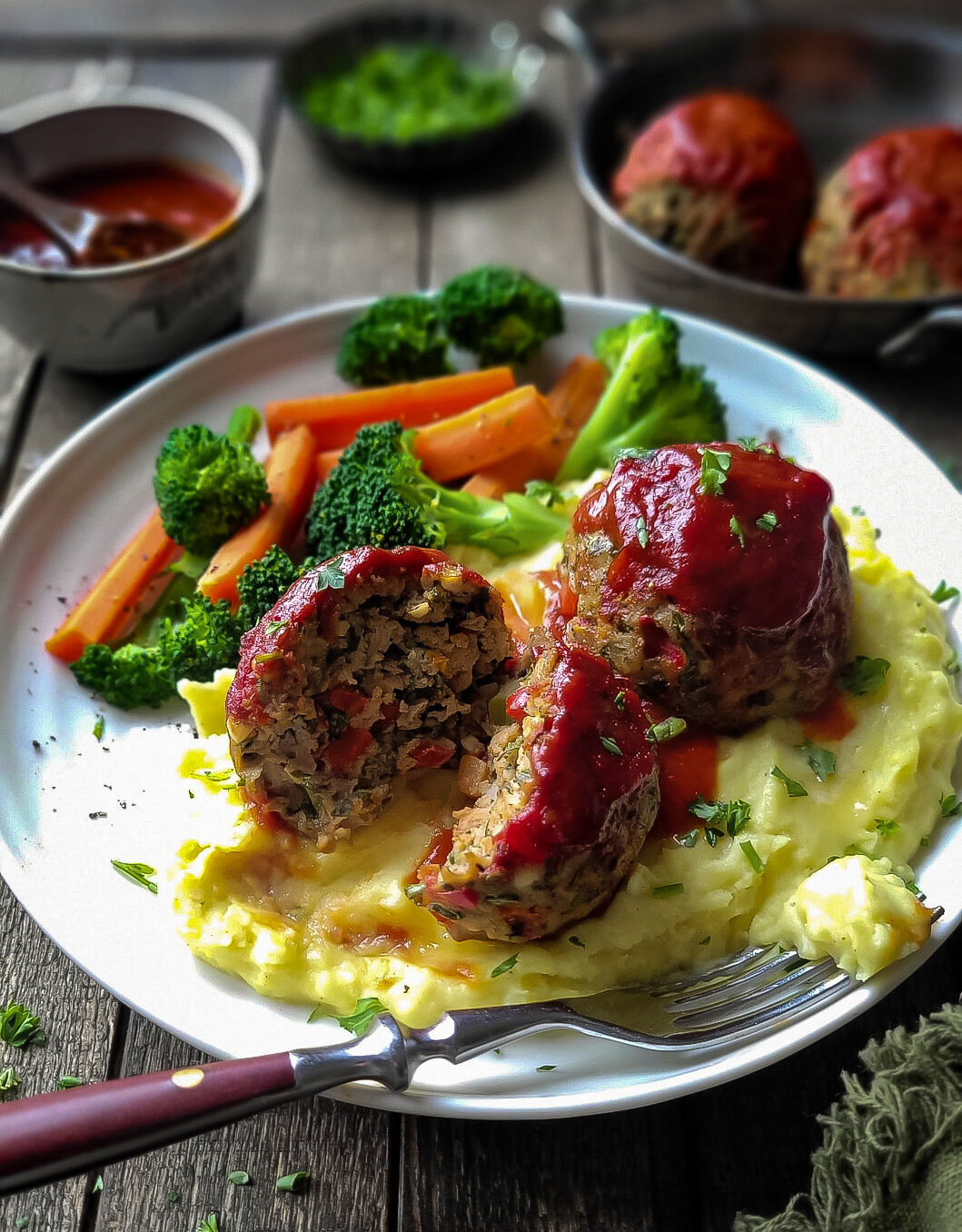 A plate filled with Brown Butter Mashed Potatoes, with two large glazed Turkey Meatloaf Balls on top, with steamed veggies to the side.