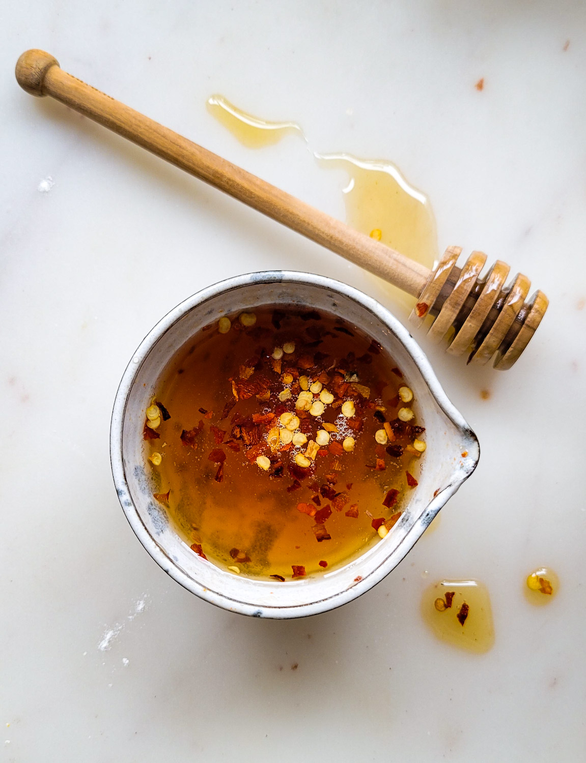 A bowl of Hot Honey and a wooden honey drizzle stick are sitting on the counter.