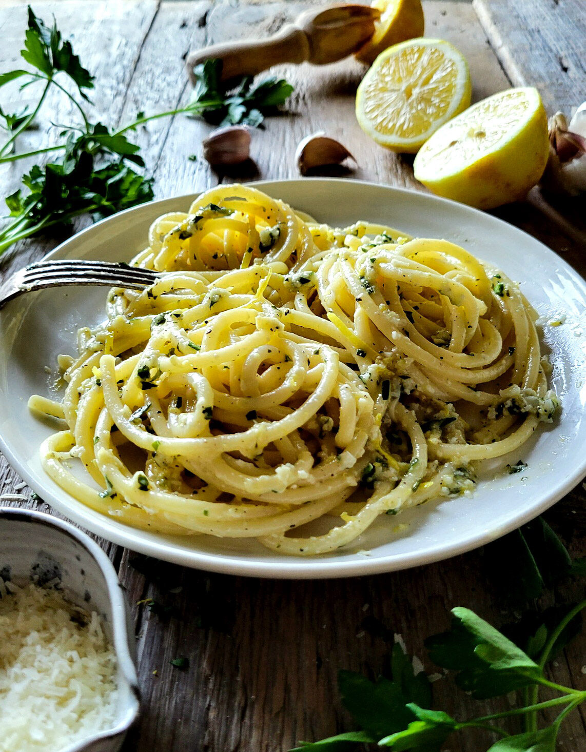 A plate of buttery, garlicky Lemon Pasta, surrounded by sliced lemon, garlic cloves, parmesan cheese and parsley.