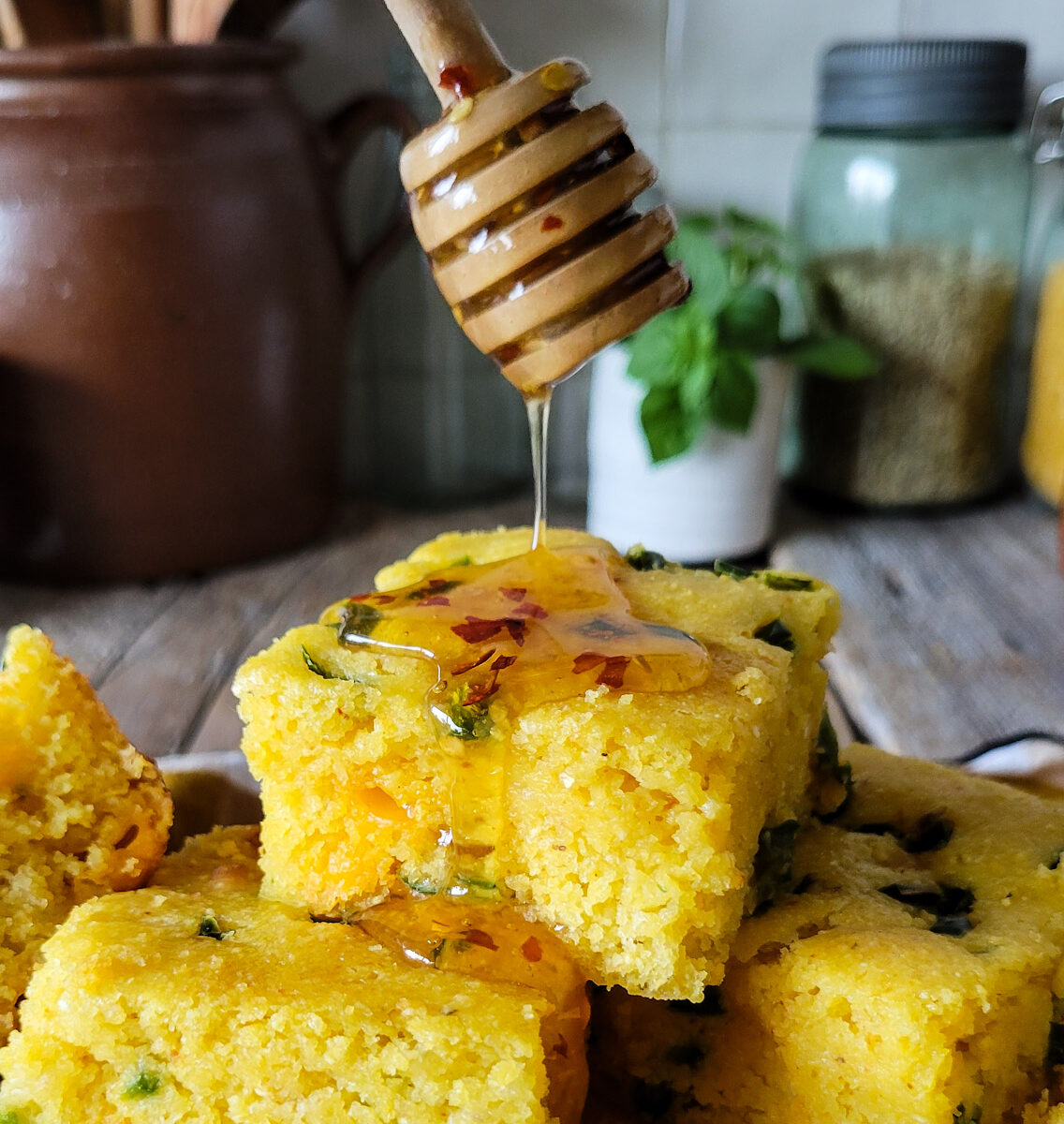 Slices of Jalapeno Cheddar Cornbread on a plate, with hot honey being drizzled over them.