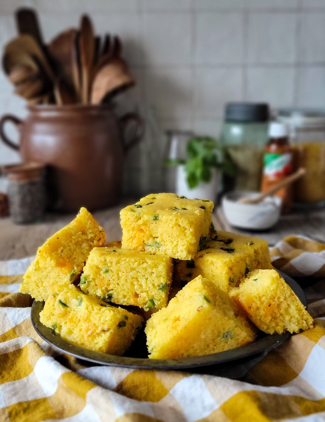 A plate of Jalapeno Cheddar Cornbread on the counter with Hot Honey in a cup in the background.