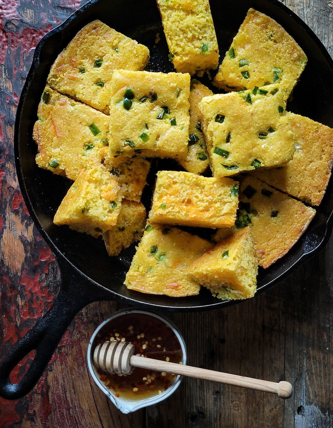 Jalapeno Cheddar Cornbread sliced up and sitting in an iron skillet with a jar of hot honey on the side.