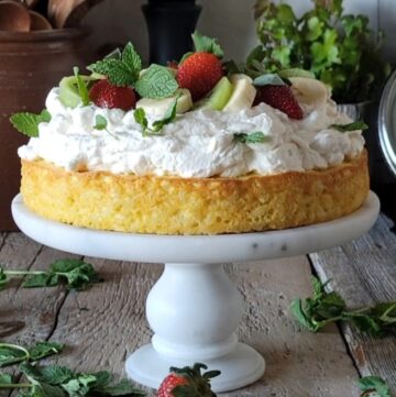 Rice Pudding Cake on a cake stand, topped with whipped cream and fresh fruit.
