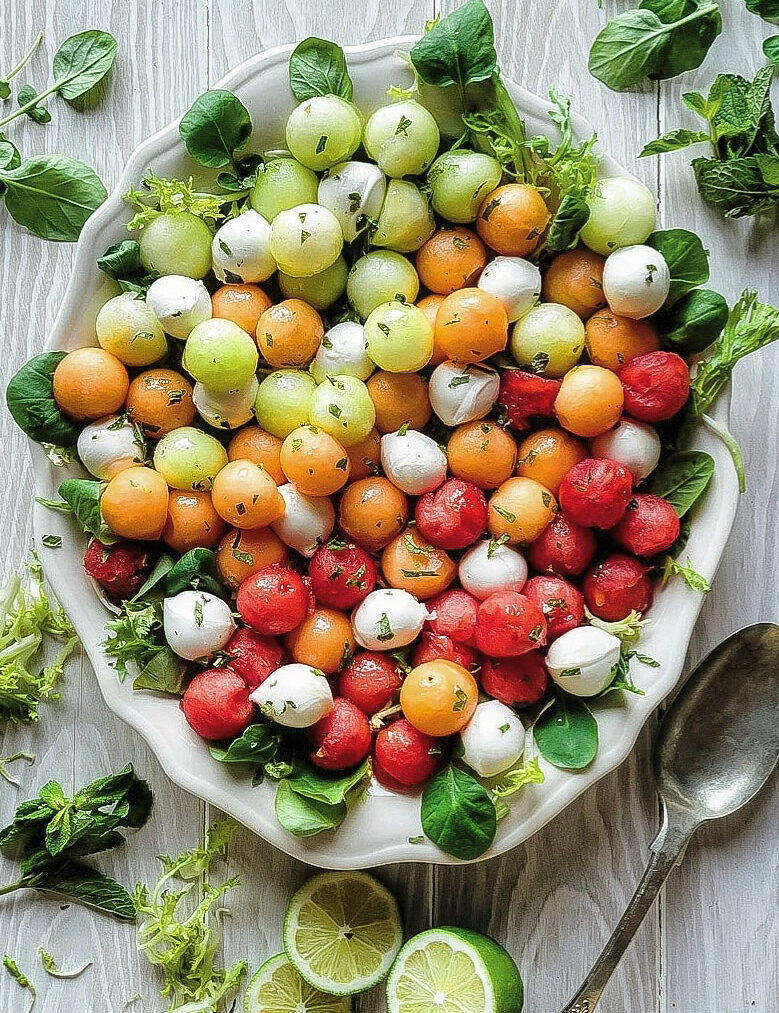 A platter filled with Agua Fresca Melon Salad. Lime slices and salad greens are scattered around.