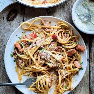 A plate with pasta and salmon tossed in a Creole Cream Sauce, with a bowl of parmesan cheese nearby.