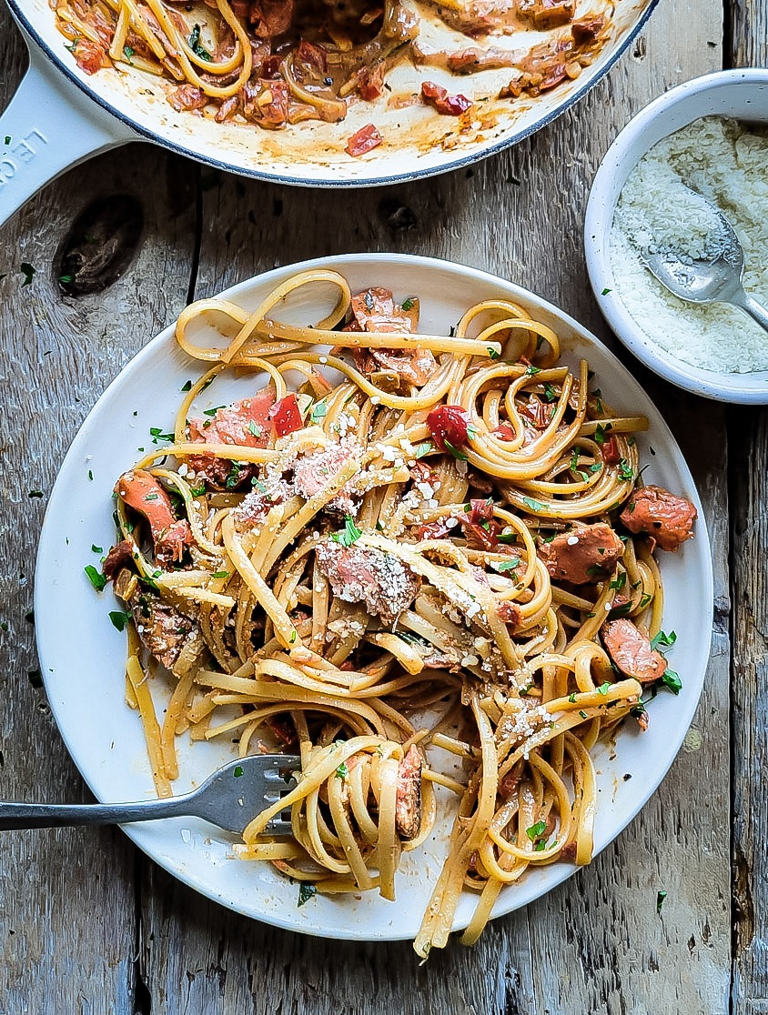 A plate with pasta and salmon tossed in a Creole Cream Sauce, with a bowl of parmesan cheese nearby.