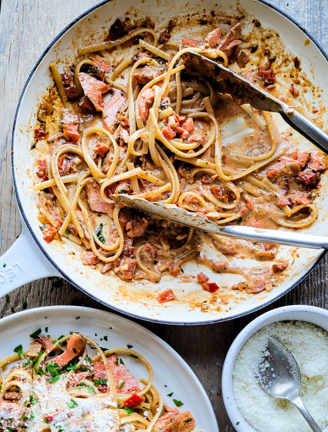 A skillet filled with pasta and salmon tossed in a Creole Cream Sauce, with a serving on a plate nearby.