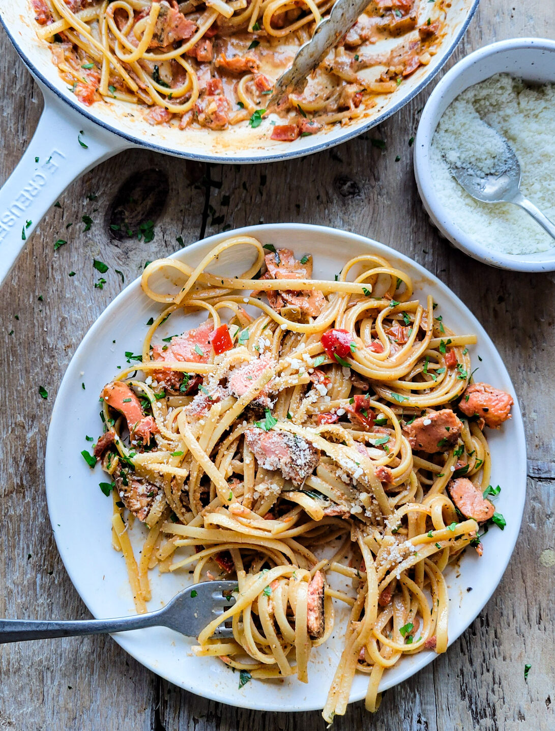 A serving of pasta and salmon tossed in a Creole Cream sauce, with a bowl of parmesan cheese nearby.