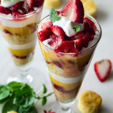 Looking down into two perfectly made Basil Strawberry Shortcake Parfaits in tall glasses.