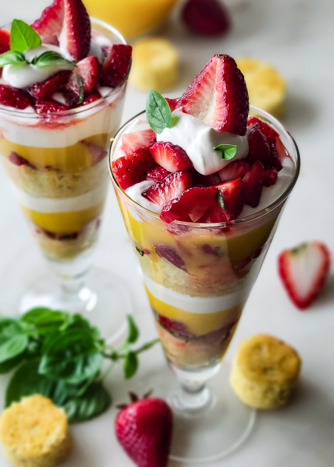 Looking down into two perfectly made Basil Strawberry Shortcake Parfaits in tall glasses.