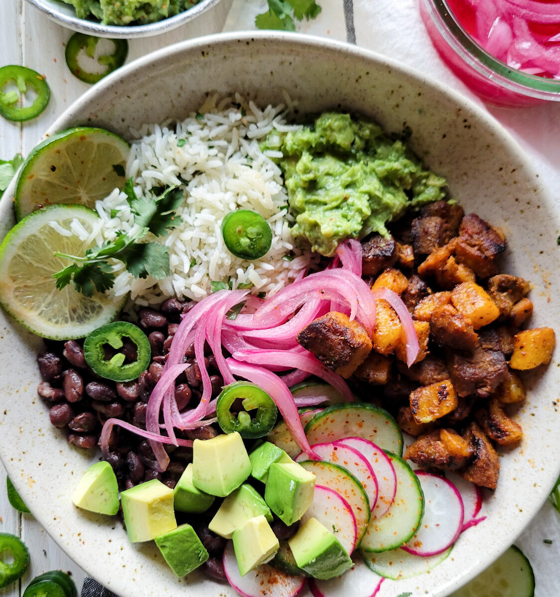 A finished bowl with all the ingredients for an Al Pastor Taco Bowl. Cilantro Rice, black beans, grilled pork and pineapple, guacamole and pickled onions round out the meal.