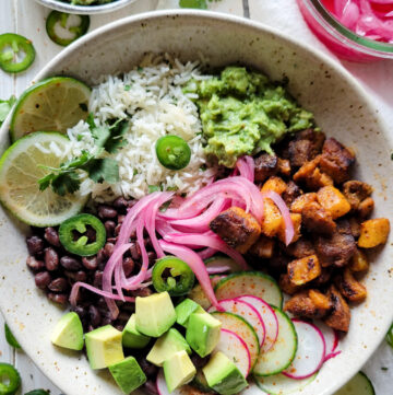 A finished bowl with all the ingredients for an Al Pastor Taco Bowl. Cilantro Rice, black beans, grilled pork and pineapple, guacamole and pickled onions round out the meal.