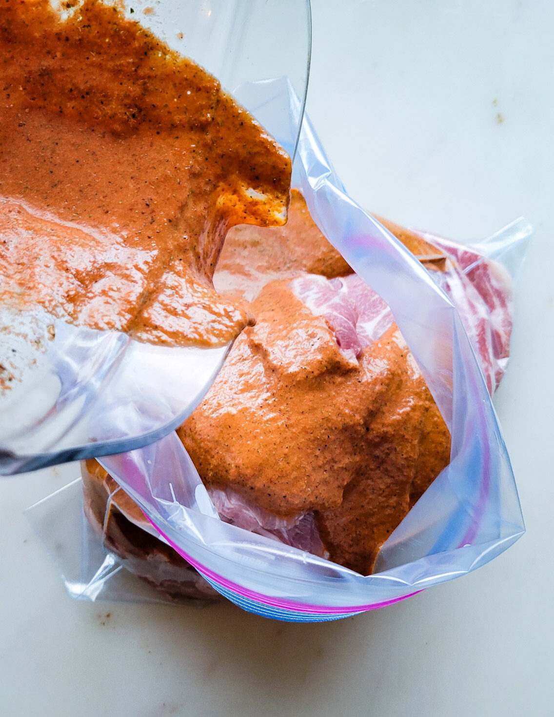 Pouring marinade for Al Pastor Taco Bowl over sliced pork placed into a freezer bag.