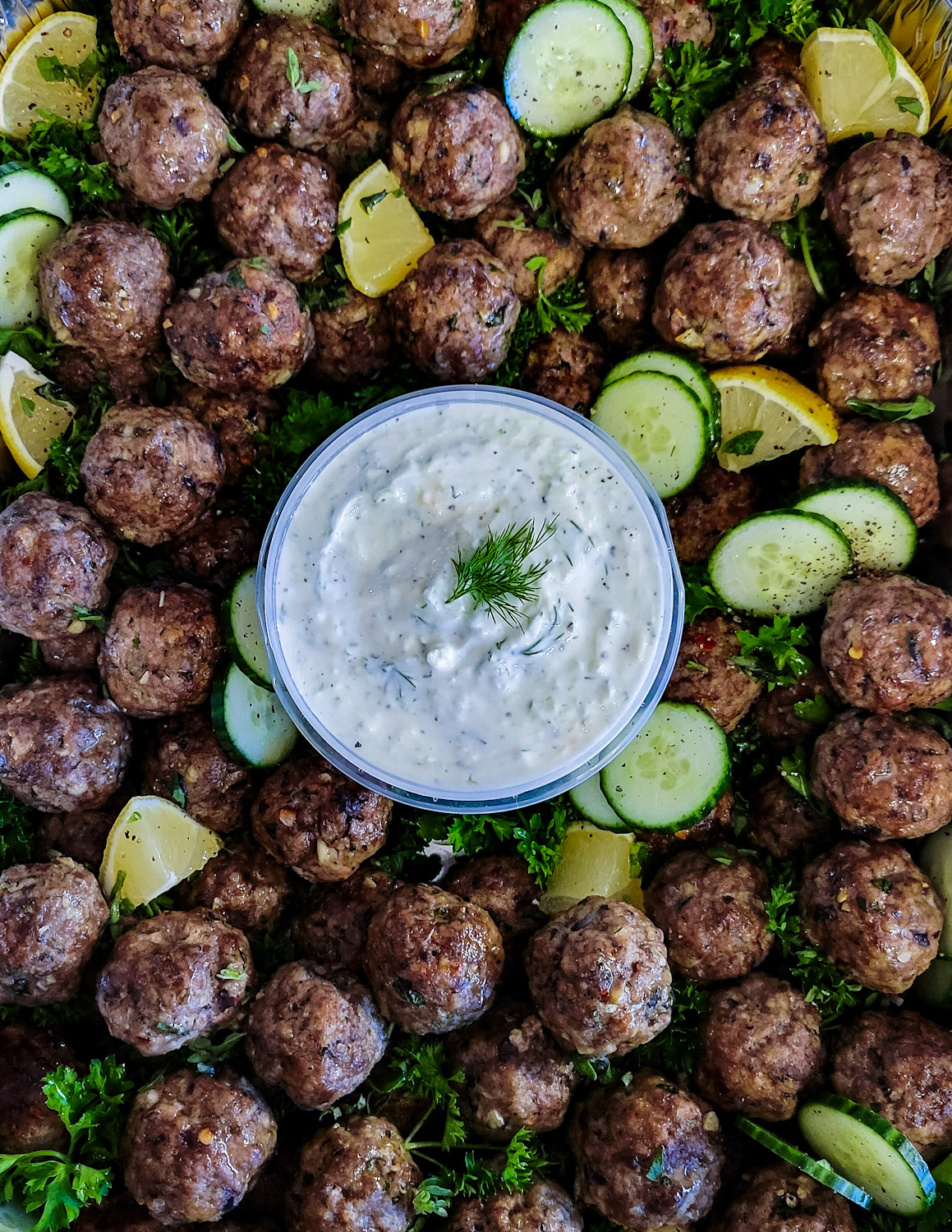 A platter filled with Feta Stuffed Greek Meatballs and a bowl of Labneh Tzatziki.