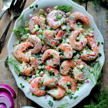 Nordic Shrimp Salad on a platter surrounded by fresh dill, cucumbers and red onions.