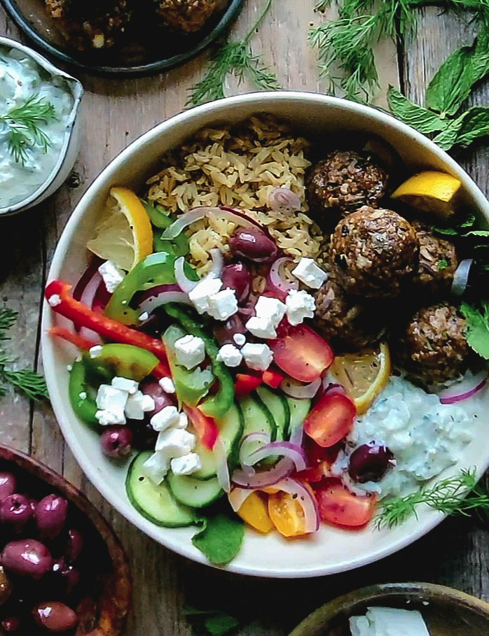 Feta Stuffed Greek Meatballs Bowl surrounded by olives and Tzatziki.