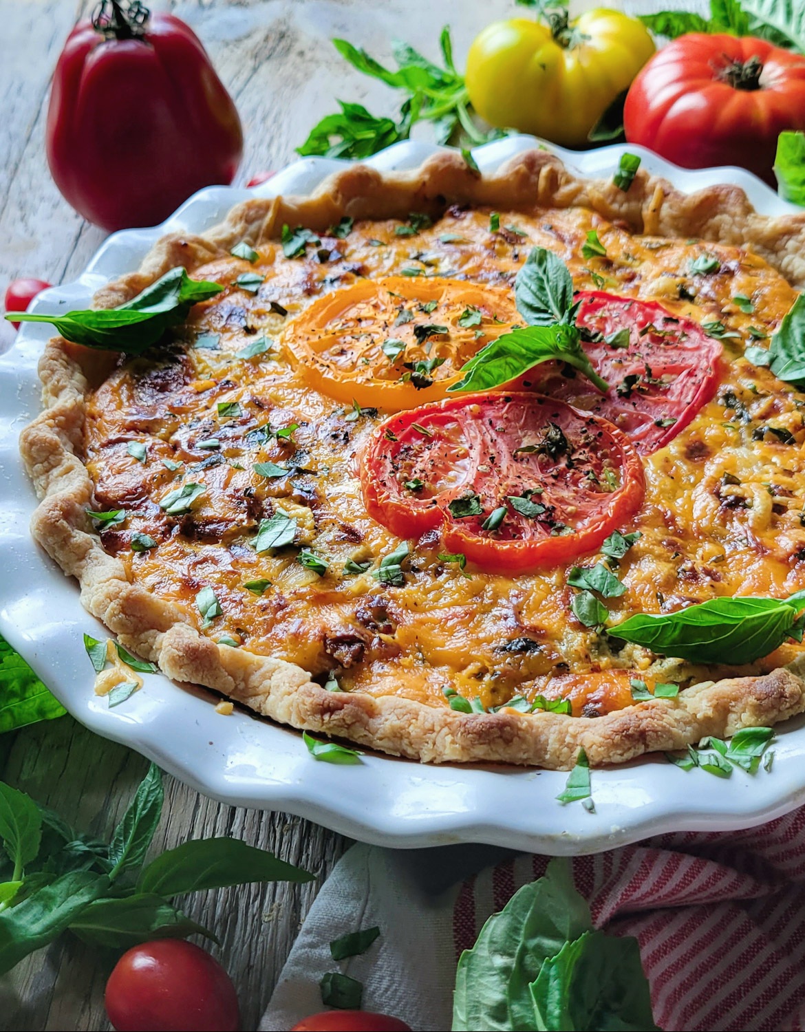 A fully baked Cheesy Tomato Pie cooling on the counter surrounded by fresh tomatoes and basil.