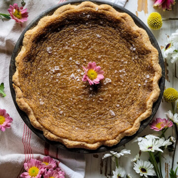 A Salty Tarte au Sucre or Sugar Pie is ready to be cut, wild flowers surround it on the counter.
