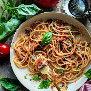A bowl of Spaghetti with fresh Summer Sauce is surrounded by fresh basil, tomatoes and a cheese grater.