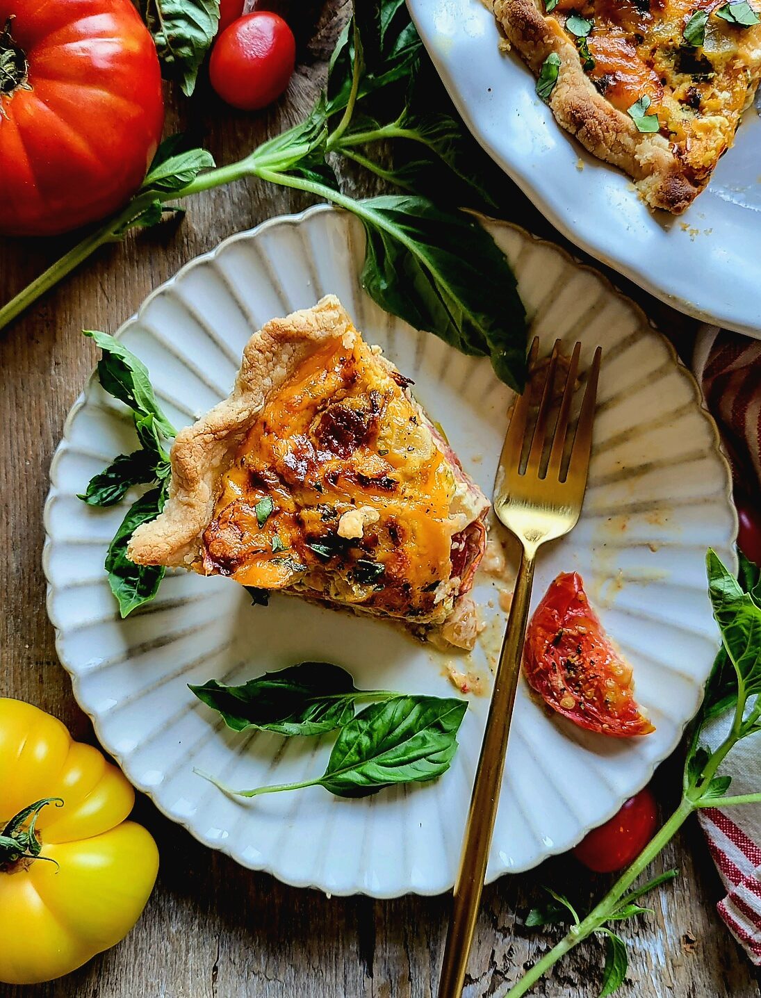 A slice of Cheesy Tomato Pie on a plate, with tomatoes and basil strewn about.