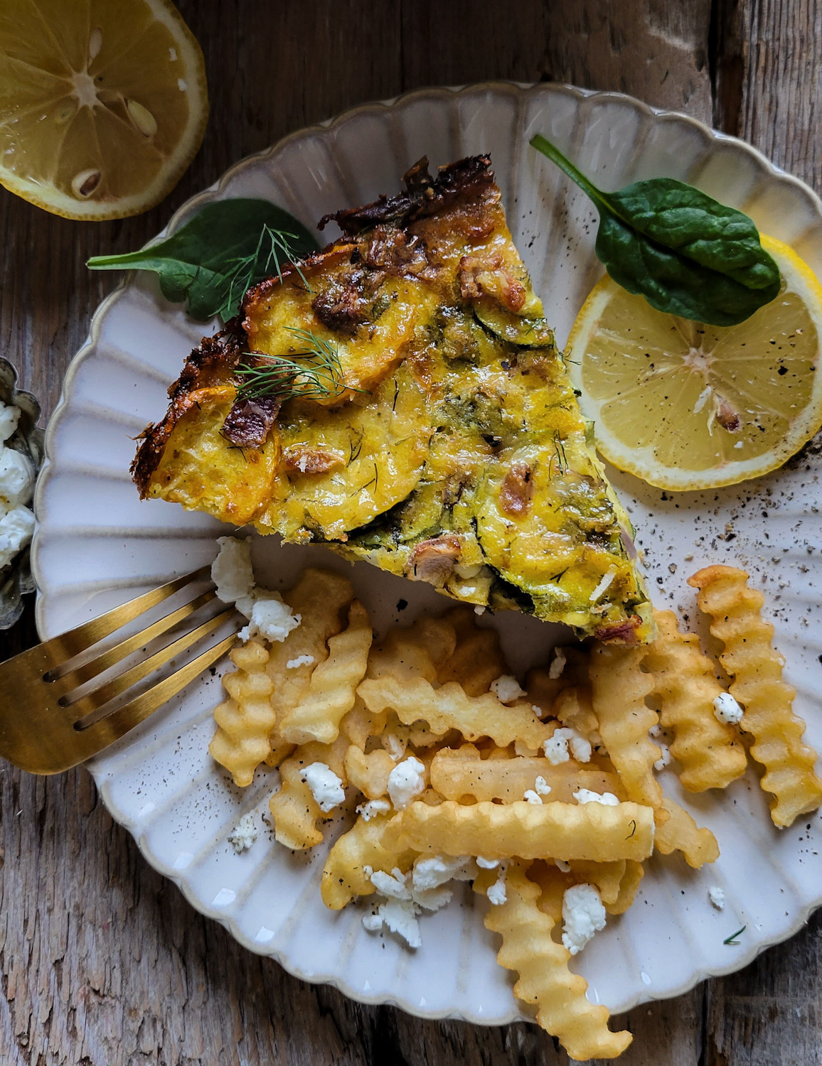 A slice of Zucchini Spanakopita Quiche served with fries and lemon on a plate.