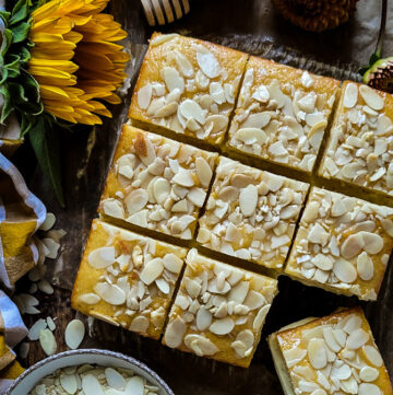 Sliced up Bienenstich Torte on a cutting board, with sunflowers and sliced almonds strewn about.