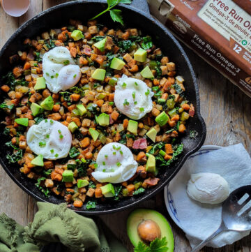 A skillet filled with Turkey Sweet Potato Hash and topped with poaches eggs. Another poached egg is on a plate, as well as avocado and and egg carton are to the side.