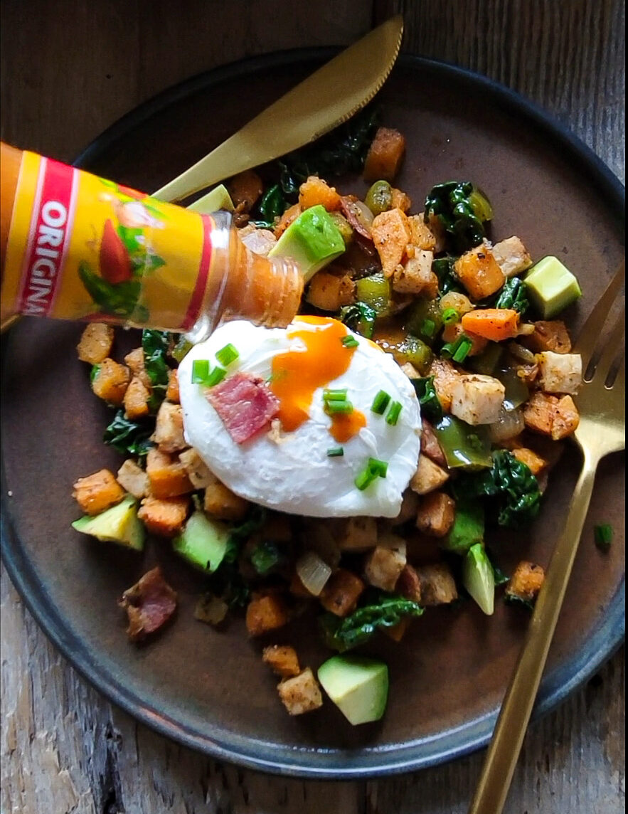 A plate with Turkey Sweet Potato Hash topped with a poached egg, with Hot Sauce being added on top.