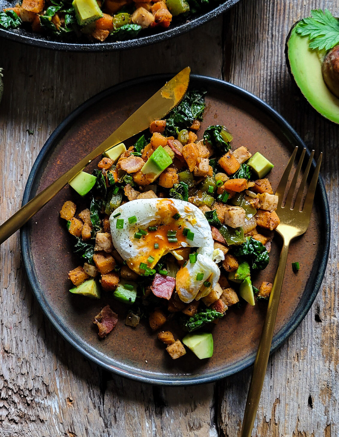 A plate of Turkey Sweet Potato Hash topped with a poached egg, with avocado to the side.