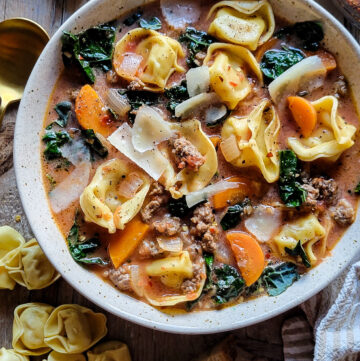 A bowl of Sausage Tortellini Soup with uncooked tortellini to the side.