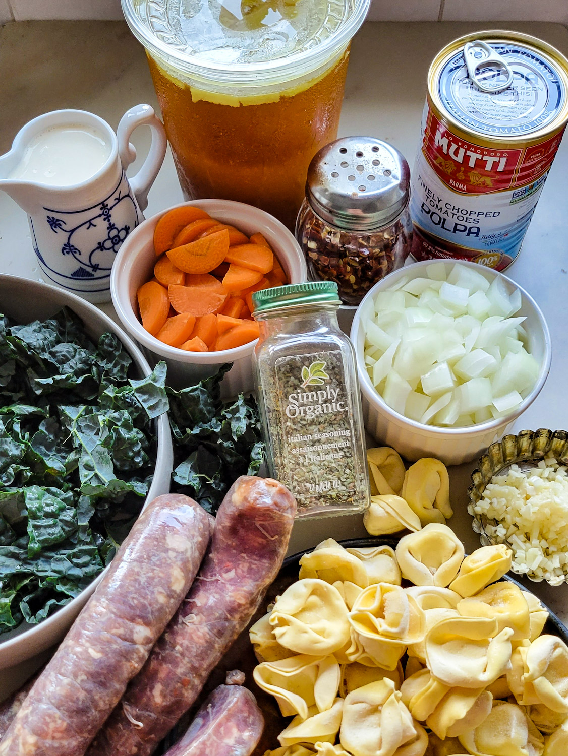 Ingredients needed to make Sausage Tortellini Soup set out on the counter.