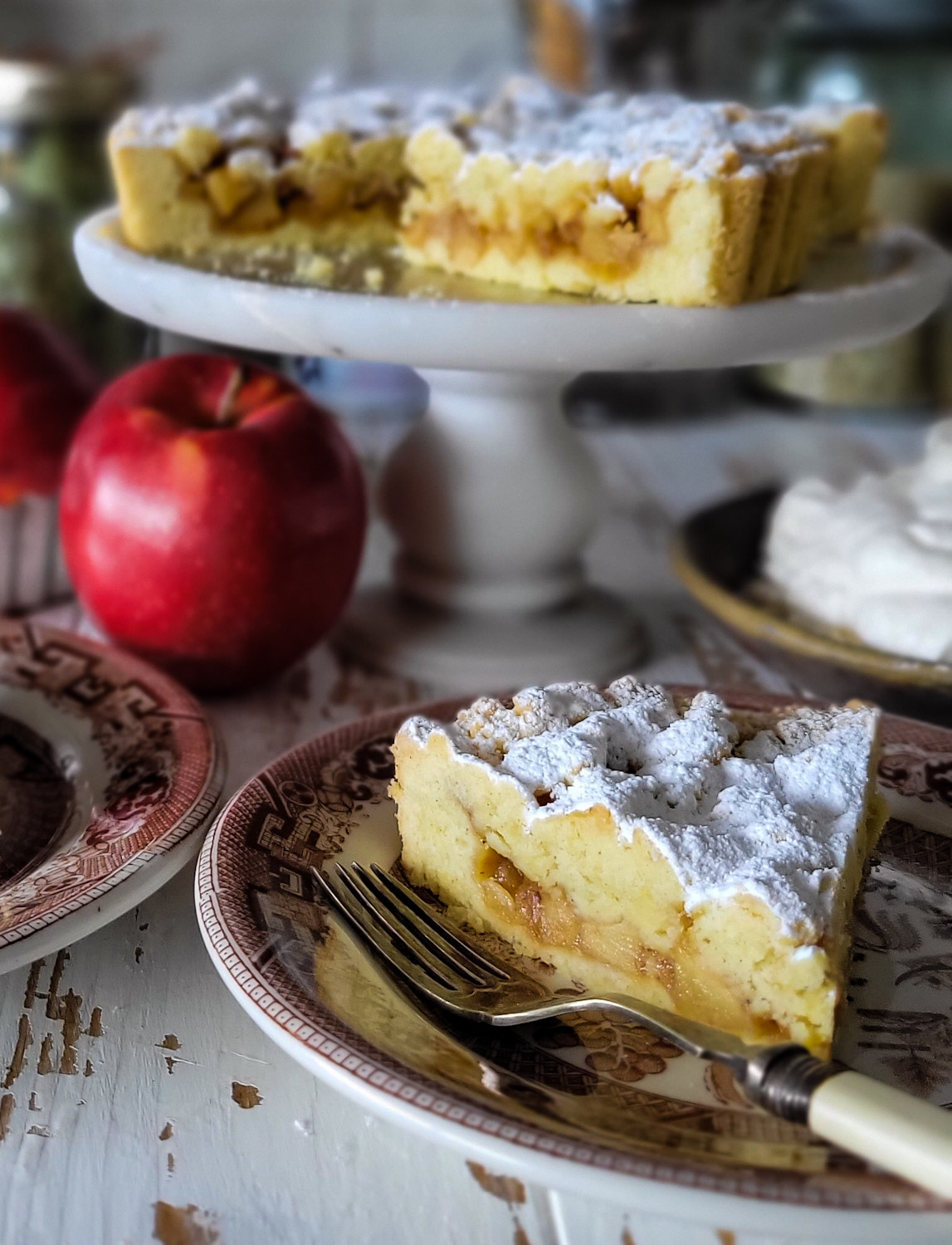 Close up of a slice of Salted Bourbon caramel Apple Crostata with the rest of the torte in the background on a cake stand.