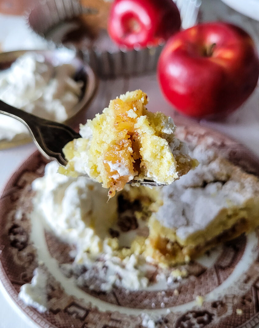 Close up of a bite of Salted Bourbon caramel Apple Crostata on a fork with the torte in the background along with some fresh red apples.