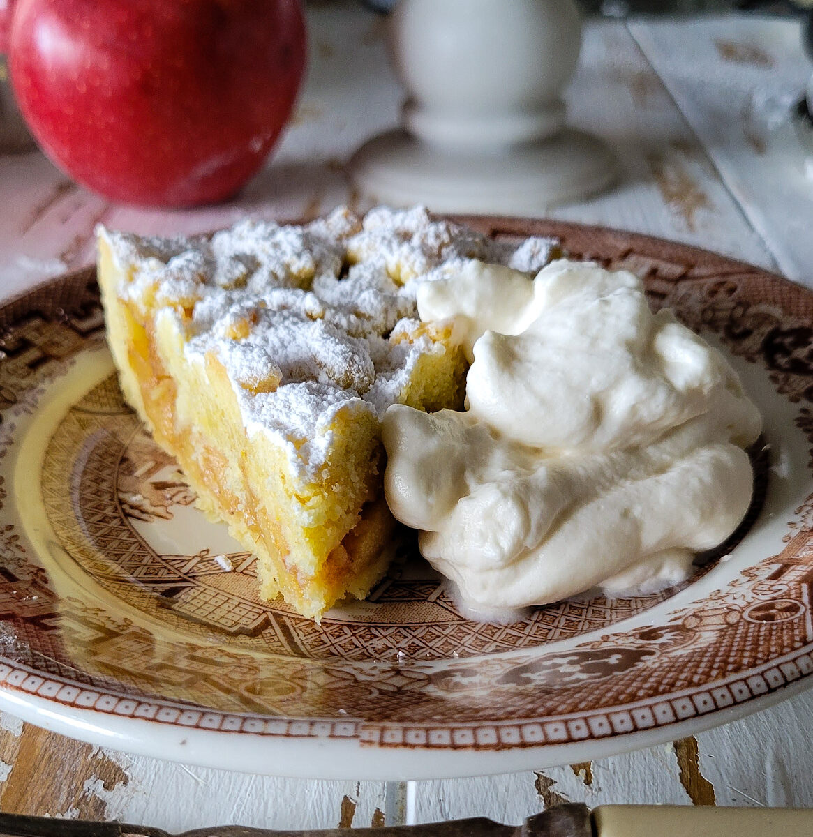 A slice of Salted Bourbon Caramel Apple Crostata on a plate along with a mound of maple whipped cream faces the camera