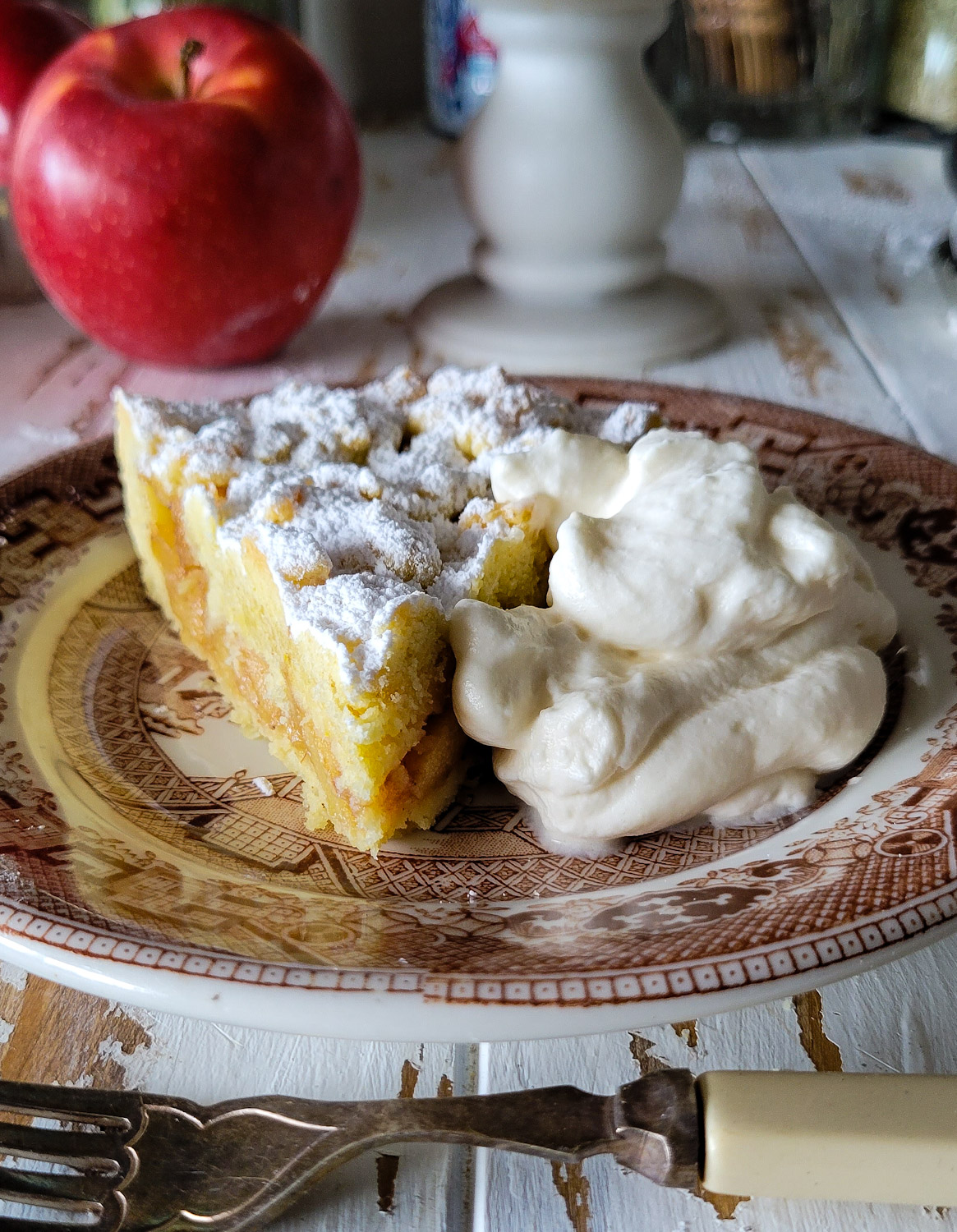 A slice of Salted Bourbon Caramel Apple Crostata on a plate along with a mound of maple whipped cream faces the camera