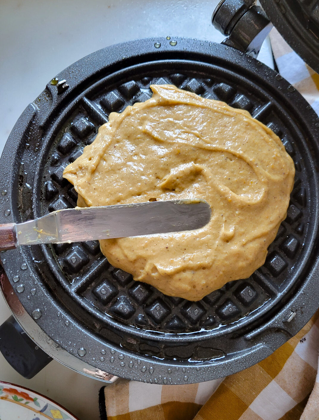 Spreading out the waffle batter in a waffle iron to make Pumpkin Waffles with Cinnamon Honey Butter