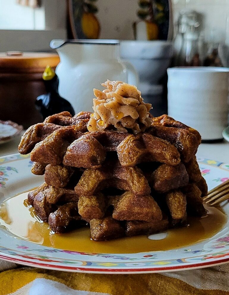 A stack of Pumpkin Waffles with Whipped Cinnamon Honey Butter on top.